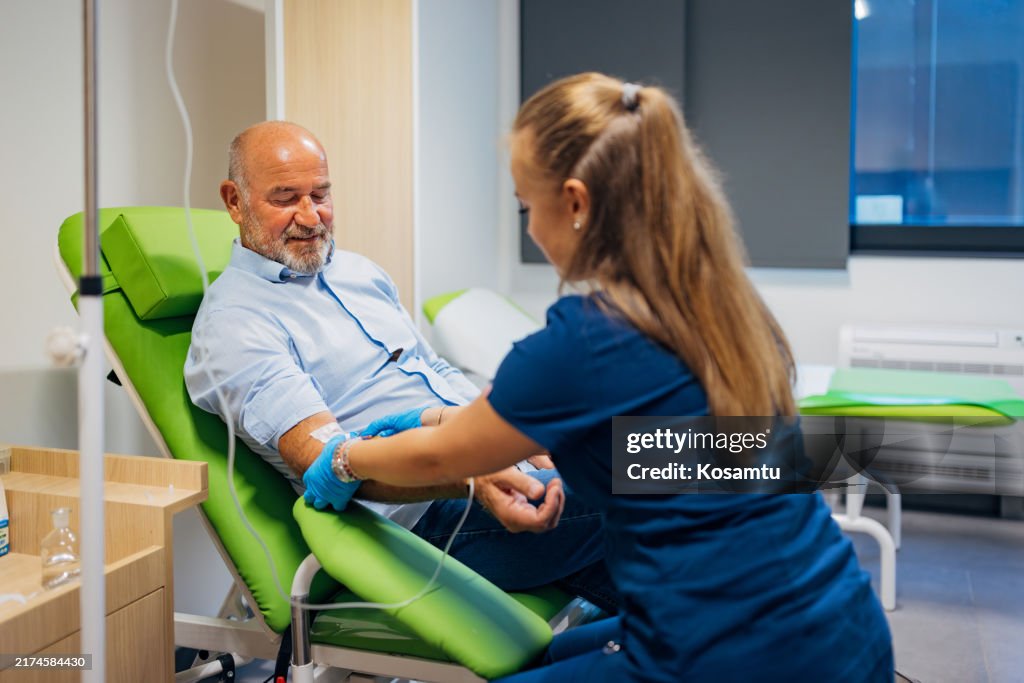 A nurse casually chats with a smiling senior patient while drawing blood from his vein for blood tests and analysis