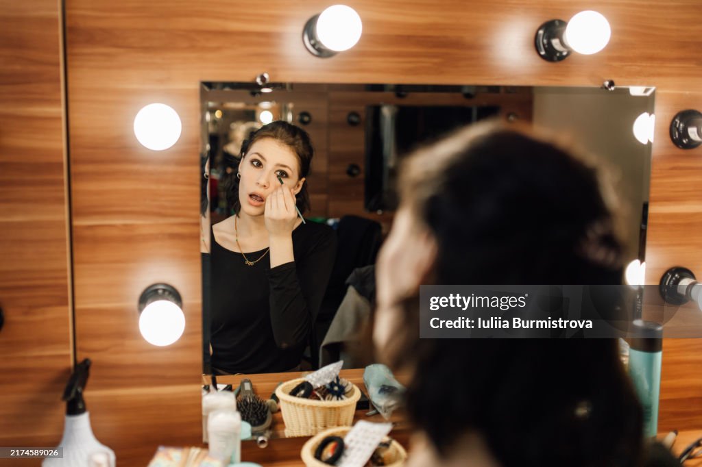 Beautiful young actress applying makeup getting ready to perform in drama play in student theater club