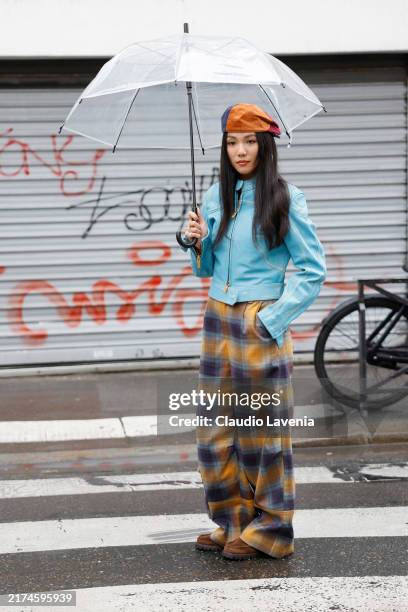 Yoyo Cao wears light blue jacket, orange red blue hat, orange and purple checked trousers, brown shoes, outside Dries Van Noten, during Womenswear...