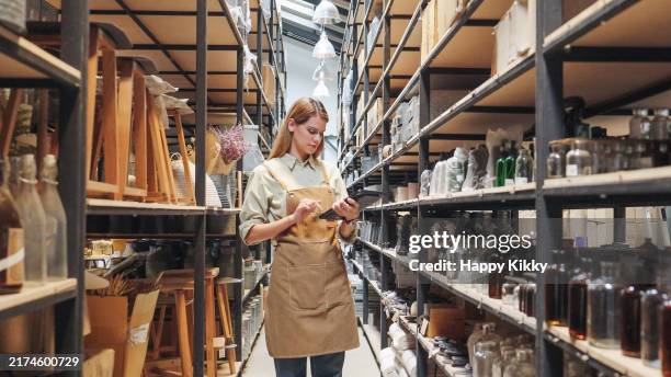 un proprietario di magazziniere di una piccola impresa che indossa grembiuli che conta controllando la gestione delle scorte sugli scaffali discutendo l'inventario in una lista di controllo del vano di stoccaggio ben organizzata - the art factory foto e immagini stock