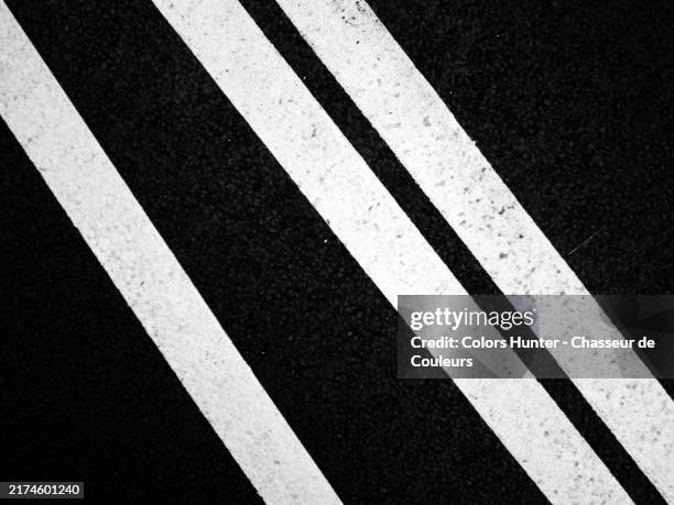 three oblique white lines on a textured black background. black and white close-up of a road marking. sunlight. paris, france. - road marking stock pictures, royalty-free photos & images