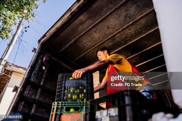 junger mann trägt kisten mit früchten in einem lastwagen - entladen stock-fotos und bilder