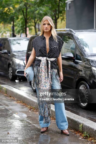 Charly Sturm wears black and white polka dot sleeveless fringed jacket, cream floral print belt scarf, blue jeans, light blue Rabanne bag, brown...