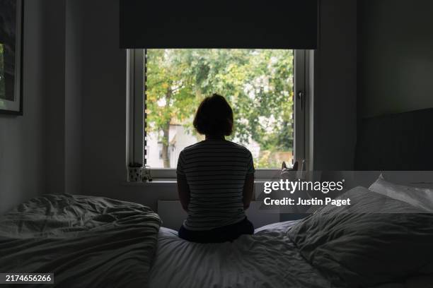 powerful rear view shot of a mature woman looking out of her bedroom window - negative emotion - in silhouette stock pictures, royalty-free photos & images