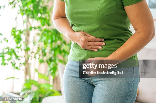 Woman touching her stomach experiencing abdominal pain at home Woman touching her stomach experiencing abdominal pain at home