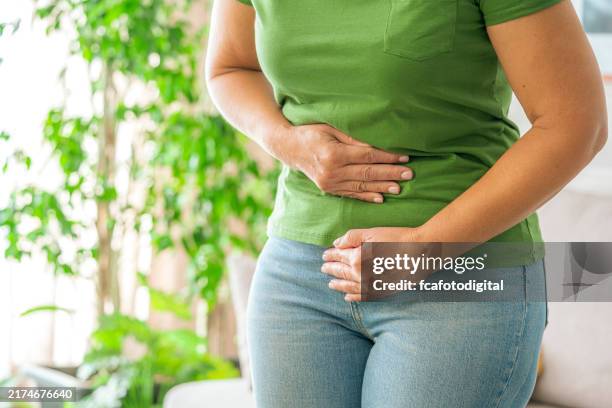 woman touching her stomach experiencing abdominal pain at home - inflamação imagens e fotografias de stock