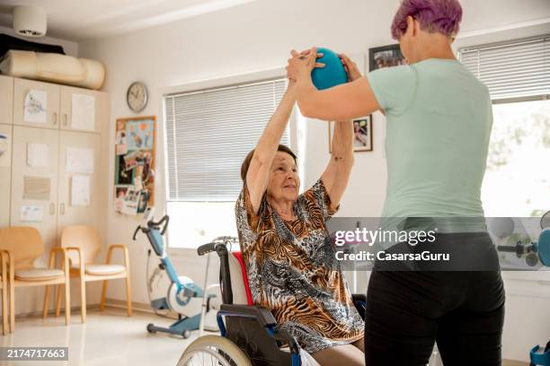 caregiver helping exercising an elderly woman in a nursing home using a soft ball - parkinsons disease stock pictures, royalty-free photos & images