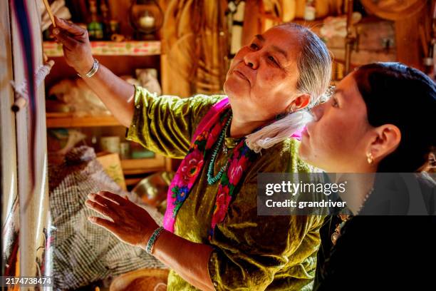 eine navajo-großmutter bringt ihrer enkelin im teenageralter bei, wie man auf einem webstuhl im monument valley webt - webstuhl stock-fotos und bilder