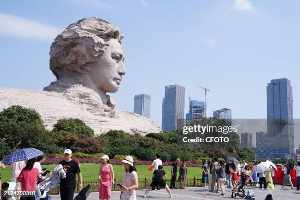 Tourists raise the five-star red flag and take photos in front of the Mao Zedong Youth Art Sculpture to celebrate China's National Day on September...