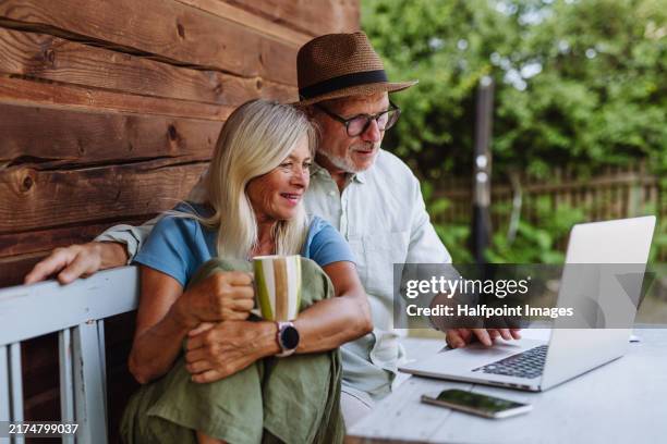 elderly woman sitting beside her senior husband who is working on laptop. - electronic banking stock pictures, royalty-free photos & images