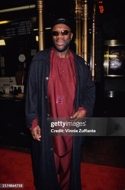 American singer and songwriter Isaac Hayes, wearing a full-length black coat over a deep red outfit, and sunglasses, attends the Hollywood premiere...