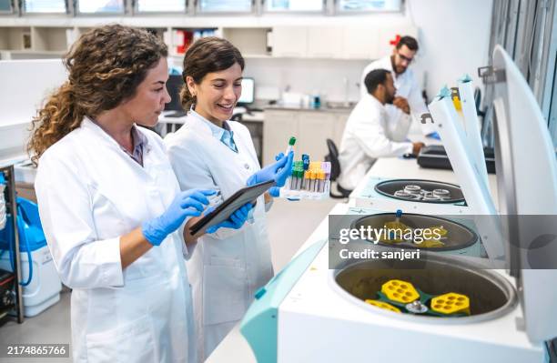 konzentrierte laborantinnen analysieren daten auf dem tablet - medizinische forschung stock-fotos und bilder