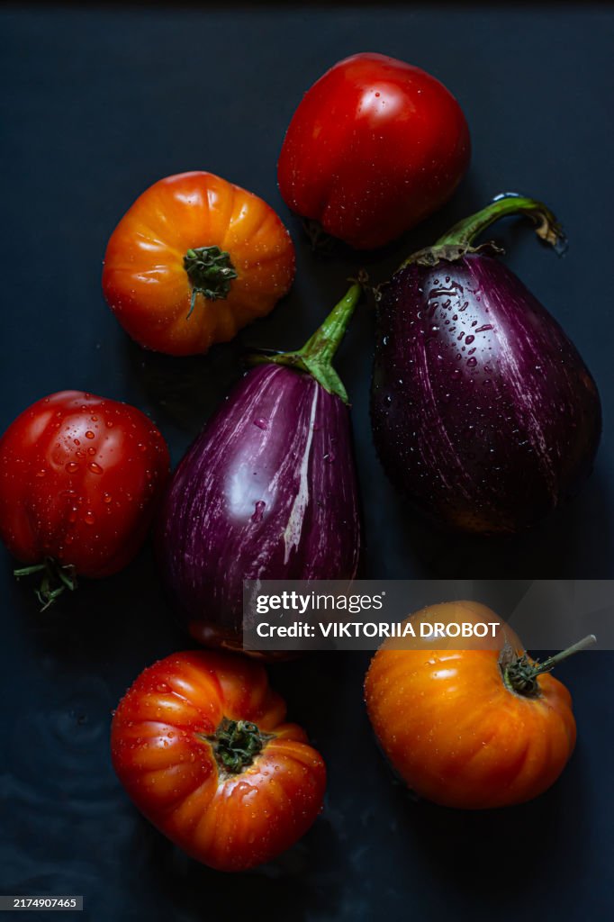 Fresh ripe tomatoes and eggplants on a dark background. Healthy vegetables. Top view of vegetables assortment