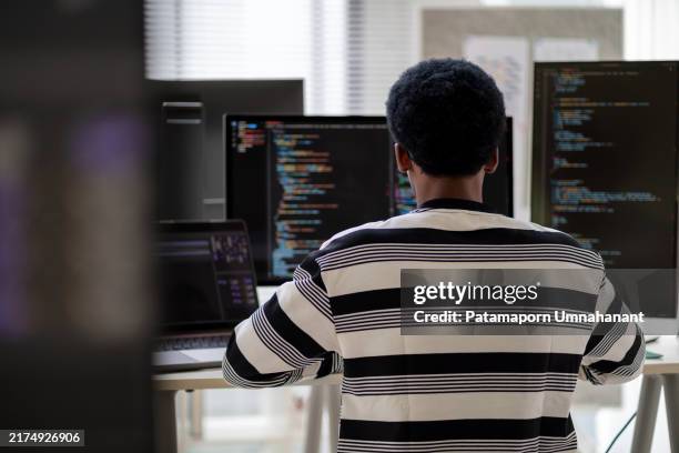 afroamerikanische männliche entwickler beschäftigen sich in einem modernen büro mit programmierung und netzwerksicherheit. der entwickler arbeitet an einem laptop und analysiert eine dashboard-schnittstelle. problemlösung in einer hybriden arbeitsumgeb - programmierschnittstelle stock-fotos und bilder