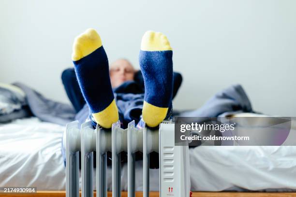 man warming feet on electric heater at home - voet stockfoto's en -beelden