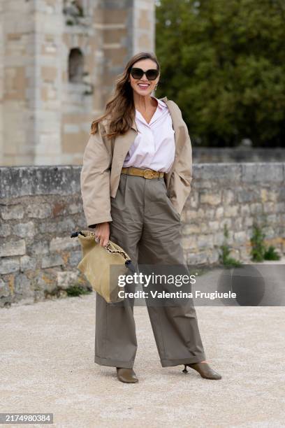 Guest wears brown sunglasses, a white shirt, a suede beige belt, a beige short trench, khaki high waist trousers, olive green leather heeled ankle...
