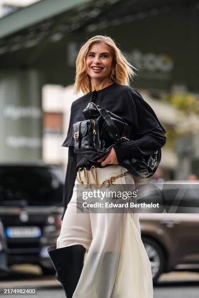 Xenia Adonts wears black long sleeve shirt, shiny black Chloe leather bag, gold Chloe belt, white sheer mesh flowy asymmetrical Chloe midi skirt,...