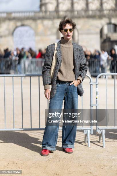 Guest wears beige sunglasses, blue jeans, red sneakers, a beige turtle neck sweater, a beige bag and a checked grey blazer outside Loewe show during...