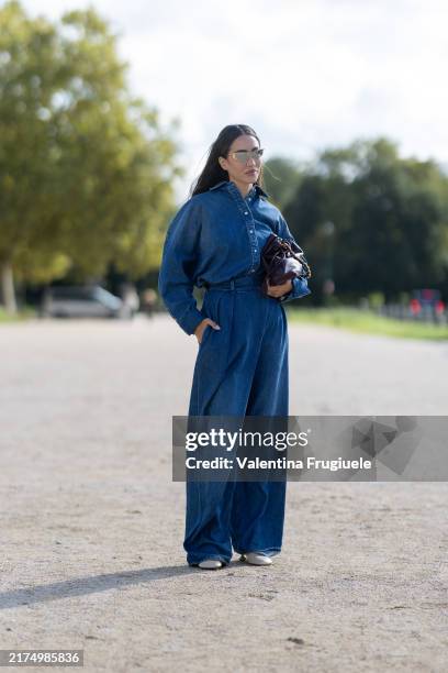 Tamara Kalinic wears white pumps, a burgundy leather bag, gold sunglasses, silver earrings and a denim jumpsuit outside Loewe show during Womenswear...