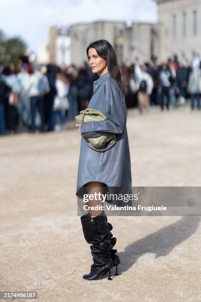 Guest wears a grey leather long sleeved shirt dress, a military green leather bag and black heeled leather knee high boots outside Loewe show during...