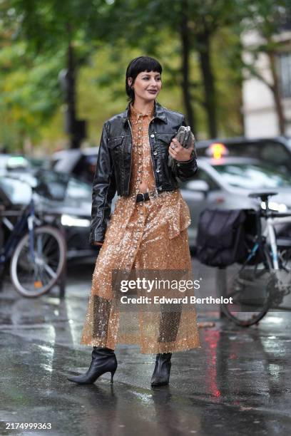 Maria Bernad wears shiny black leather jacket, dark orange sheer mesh sequin midi dress, black leather belt, shiny black pointed toe leather heels,...