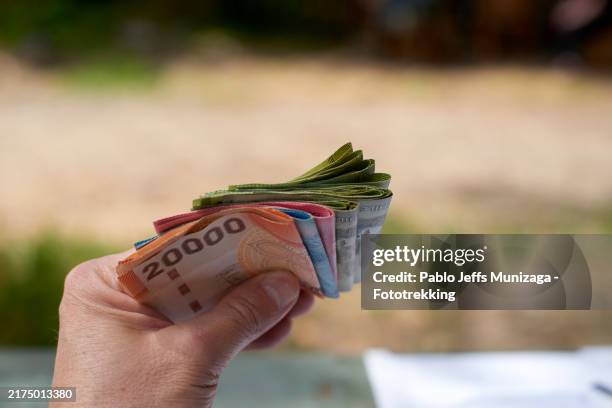 hand holding folded stack of colorful currency notes - dinheiro imagens e fotografias de stock