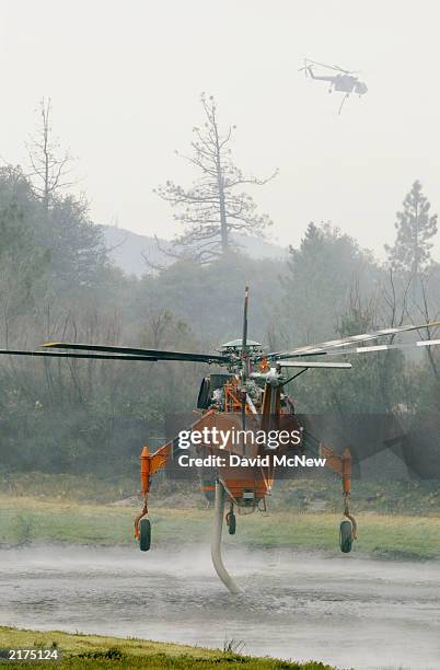 Two firefighting helicopters pick up loads of water from a pond at the Lost Valley Boy Scout Camp as the Coyote Fire burns more than 13,000 acres of...