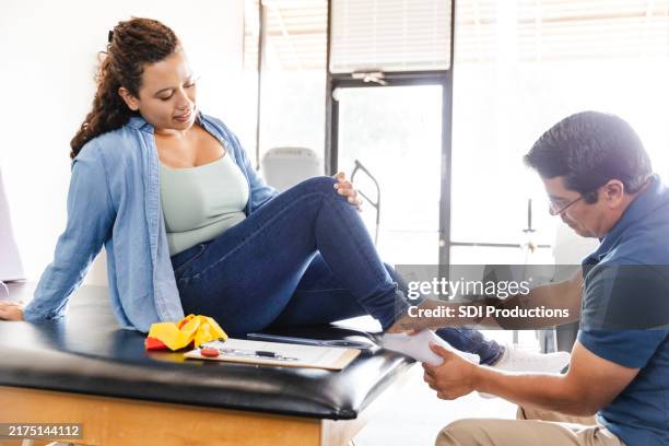 male therapist gently touches woman's injured foot - sprain stock pictures, royalty-free photos & images