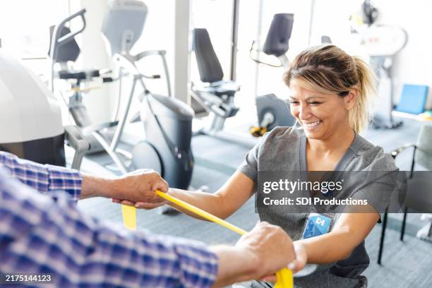 fröhliche ergotherapeutin hilft älterem mann mit widerstandsband - ambulante behandlung stock-fotos und bilder