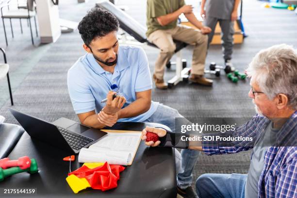 male occupational therapist discusses wrist injury with male senior patient - ergotherapie stockfoto's en -beelden