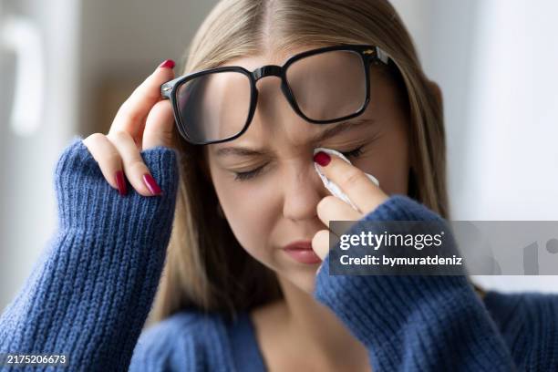 mujer joven con gafas secándose las lágrimas - miopía fotografías e imágenes de stock
