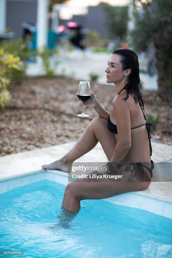 A woman with glass of wine spends time by the pool in holiday camping area.