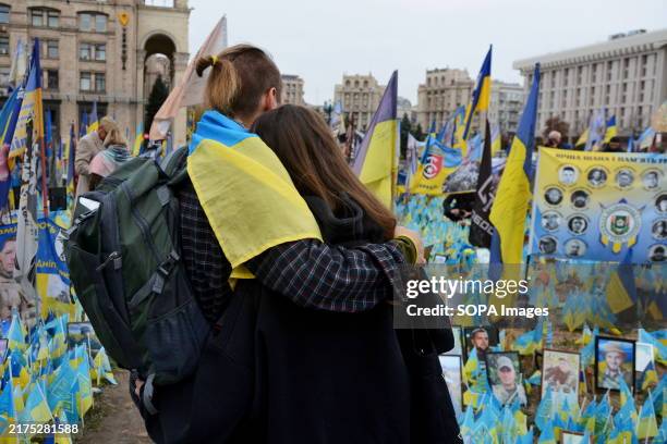 Couple of people wrapped in the Ukrainian flag stand among the flags near a makeshift memorial to fallen Ukrainian soldiers in Kyiv. Today, Ukraine...