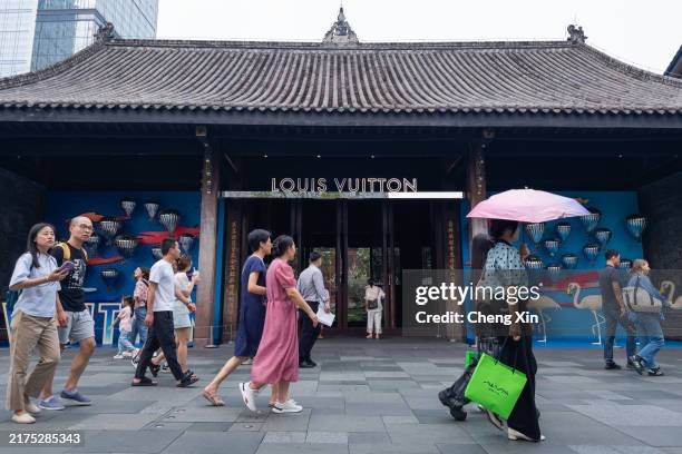Pedestrians walk past a Louis Vuitton store in Chengdu, housed in a traditional-style building with modern branding and colorful displays visible...