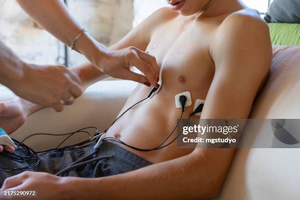 mother adjusts ecg holter monitor to check child's heart health at home - hartritmestoornis stockfoto's en -beelden