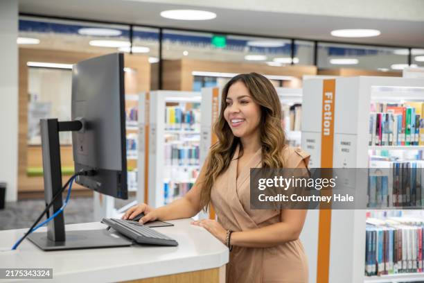 una donna sorridente controlla il computer della biblioteca per trovare il titolo di un libro. - bibliotecario foto e immagini stock