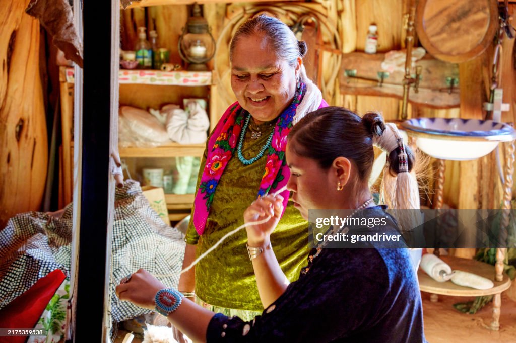 Navajo Grandmother Teaching Her Teenage Granddaughter How To Weave On A Loom in Monument Valley Side View