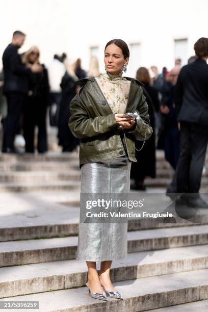 Yulia German wears silver earrings, a silver bag, a beige turtle neck floral printed sweater, a silver midi skirt, silver pumps and a military green...