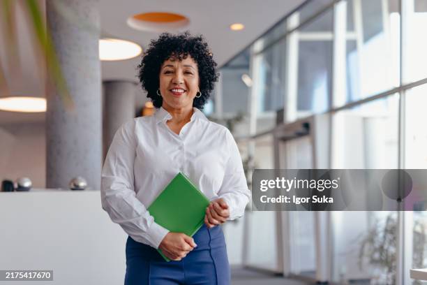 retrato de una mujer de negocios con el pelo rizado sosteniendo un cuaderno verde en una oficina moderna - director ejecutivo fotografías e imágenes de stock