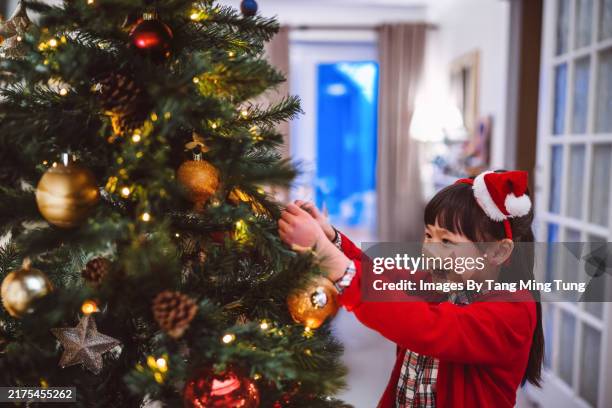 cheerful young girl decorating a christmas tree at home in festive holiday - christmas decoration stock pictures, royalty-free photos & images