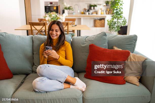 woman relaxing at home using smartphone on couch - vestido vermelho - fotografias e filmes do acervo