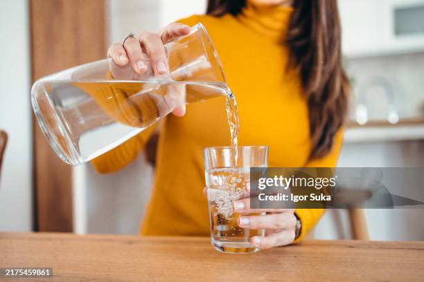 nahaufnahme einer frau, die wasser in glas in der modernen küche gießt - wasser trinken stock-fotos und bilder