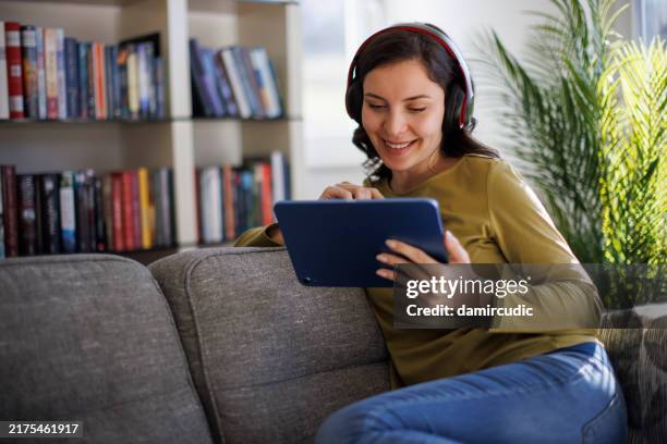 mujer sonriente relajándose con tableta digital en el sofá de casa - lector de libros electrónicos fotografías e imágenes de stock