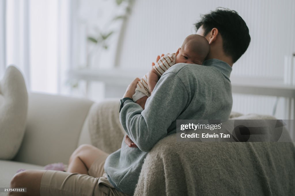 Asian chinese young father burping baby girl after milk in living room