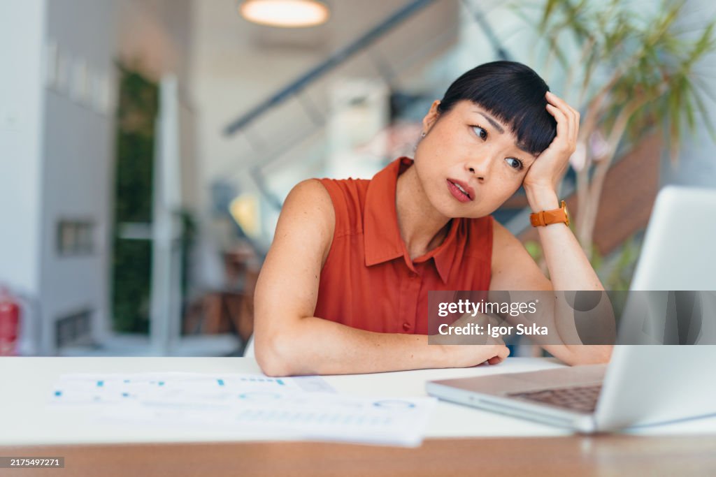 Mujer de negocios asiática estresada sentada en el escritorio con una computadora portátil en una oficina moderna
