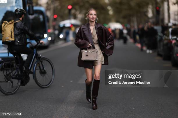 Leonie Hanne is seen wearing shiny silver earrings in a large organic shape from Alaïa; a burgundy leather coat with lapel collar from Hermès; a...