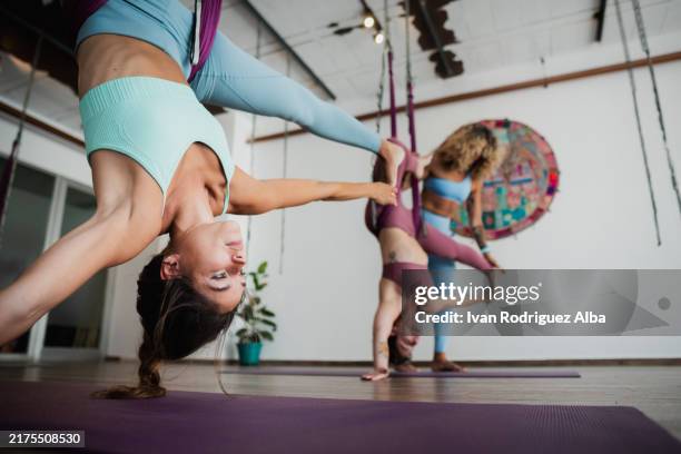 group of women doing aerial yoga poses using hammocks in a studio - acrobatiek stockfoto's en -beelden