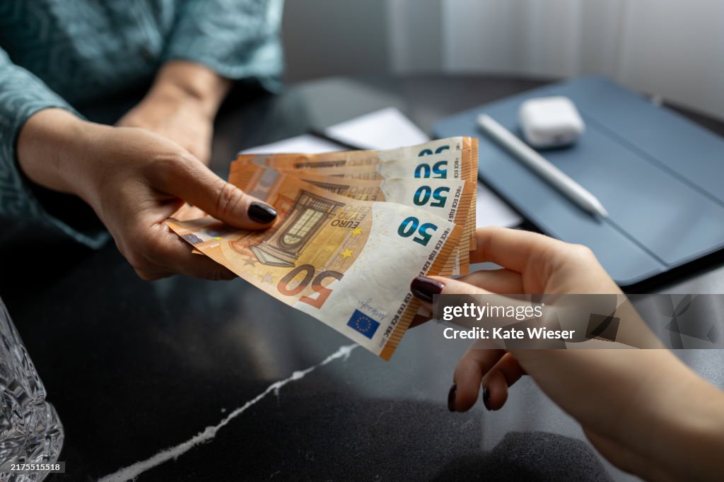Woman handing woman euro banknotes