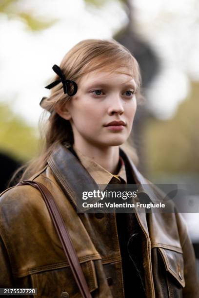 Guest wears a black velvet bow hair accessor, a beige shirt, a brown leather bag and a brown leather cargo jacket outside Valentino show during...