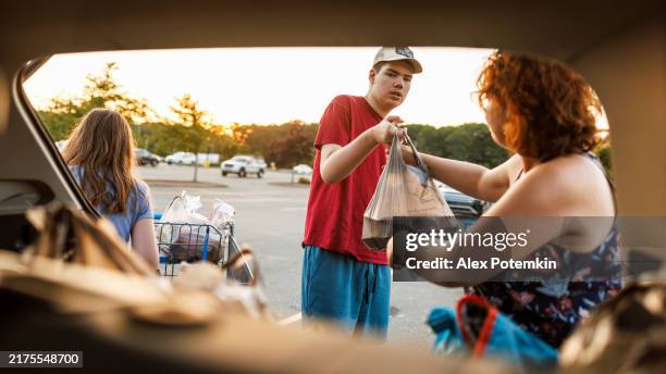 autistic teen assists mother in parking lot at sunset. - overloaded shopping cart stock pictures, royalty-free photos & images